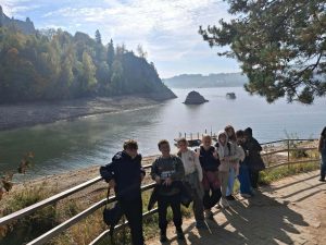 🟢 Poniedziałek – Pieniny, witajcie!
Naszą przygodę rozpoczęliśmy od spaceru malowniczym Wąwozu Homole, podziwiając jesienne barwy i wapienne skały. Nie zabrakło też wizyty w bacówce i degustacji pysznych, świeżych oscypków! Następnie zameldowaliśmy się w ośrodku Trzy Korony w Krościenku nad Dunajcem, a naszym stałym miejscem biesiadowania stała się klimatyczna Karczma Stajkowa.
🟡 Wtorek – Zamkowe legendy, jezioro i flisackie opowieści
Drugi dzień upłynął pod znakiem historii i wody. Najpierw z przewodnikiem zwiedziliśmy pełen tajemnic Zamek w Czorsztynie, skąd ruszyliśmy w rejs po Jeziorze Czorsztyńskim. Prawdziwym hitem okazał się jednak spływ przełomem Dunajca! Nasz flisak Paweł z ogromnym humorem sypał opowieściami o Janosiku i pienińskich szczytach, umilając nam zapierające dech w piersiach widoki.
🔴 Środa – Zdobywamy Trzy Korony!
To był dzień wielkiego wyzwania. Pod opieką przewodnika ruszyliśmy na szlak, by zdobyć słynne Trzy Korony! Poznaliśmy lokalne legendy, a na najwyższym wierzchołku – Okrąglicy (982 m n.p.m.) – podziwiając spektakularną panoramę gór, złapaliśmy wiatr w żagle. Co najważniejsze: wszyscy daliśmy radę! Wieczorem zmęczeni, ale szczęśliwi, świętowaliśmy ten sukces przy wspólnym ognisku z kiełbaskami i śpiewem.
🔵 Czwartek – Słowackie zabytki i powrót
Wszystko, co dobre, szybko się kończy. Ostatniego dnia pożegnaliśmy Krościenko i przekroczyliśmy granicę, by zwiedzić zabytkowy Czerwony Klasztor na Słowacji i poznać historię tutejszych zakonników.
To była piękna lekcja przyrody, historii i przede wszystkim – wspaniałej integracji. Pienińskie widoki i setki wspólnych uśmiechów zostaną w naszych sercach na bardzo długo! 🏫❤️